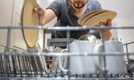 мужчина закладывает в посудомоечную машину тарелки