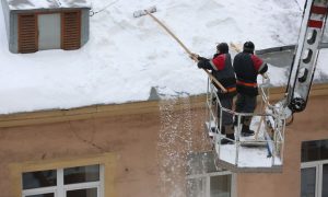 Сотрудники коммунальной службы чистят крышу жилого дома от снега.