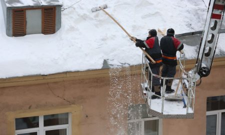 Сотрудники коммунальной службы чистят крышу жилого дома от снега.