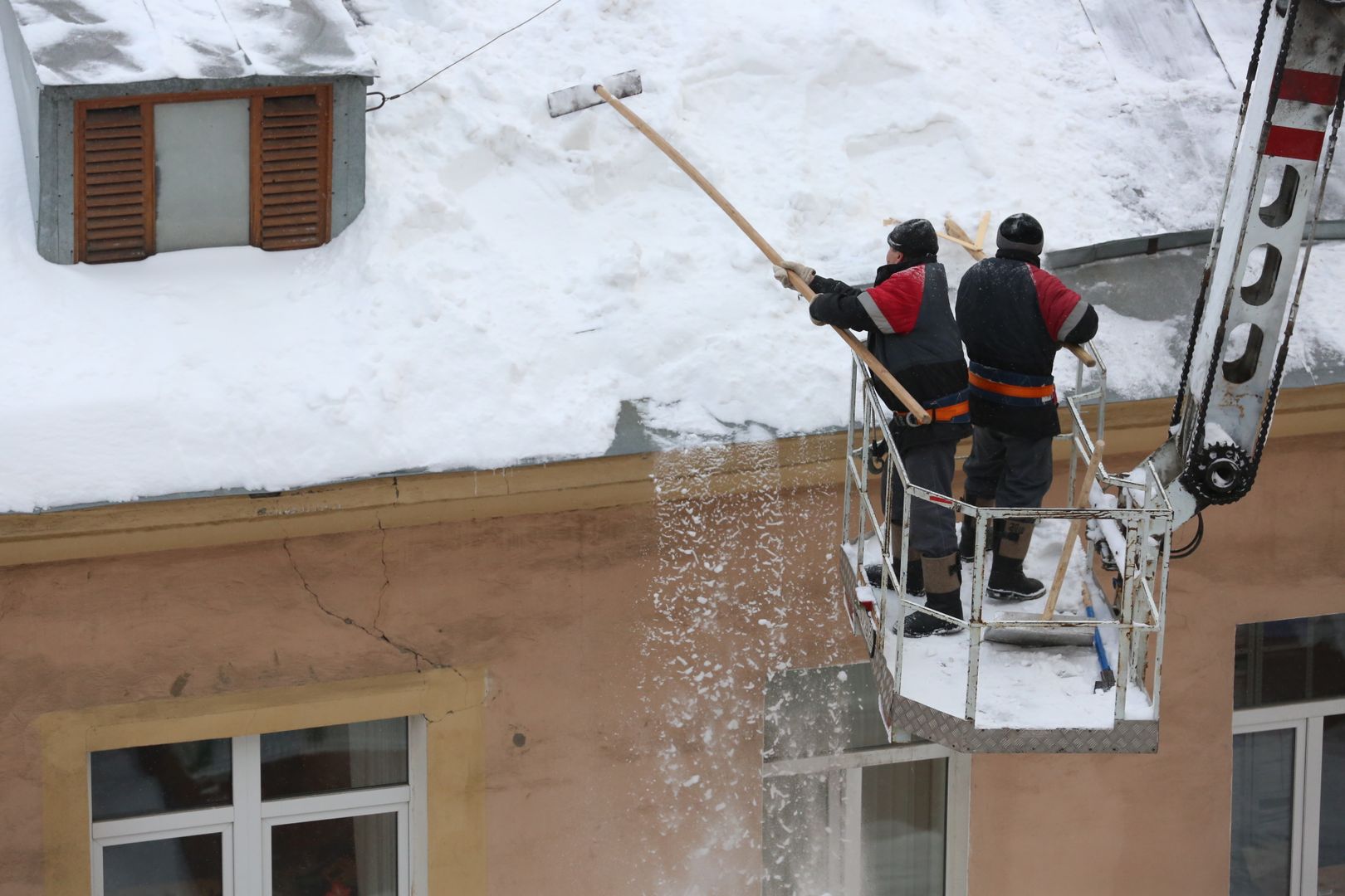 Сотрудники коммунальной службы чистят крышу жилого дома от снега.