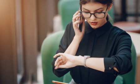 Девушка в офисной одежде разговаривает по телефону и смотрит на часы