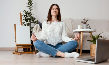 Девушка медитирует, сидя на полу перед ноутбуком.