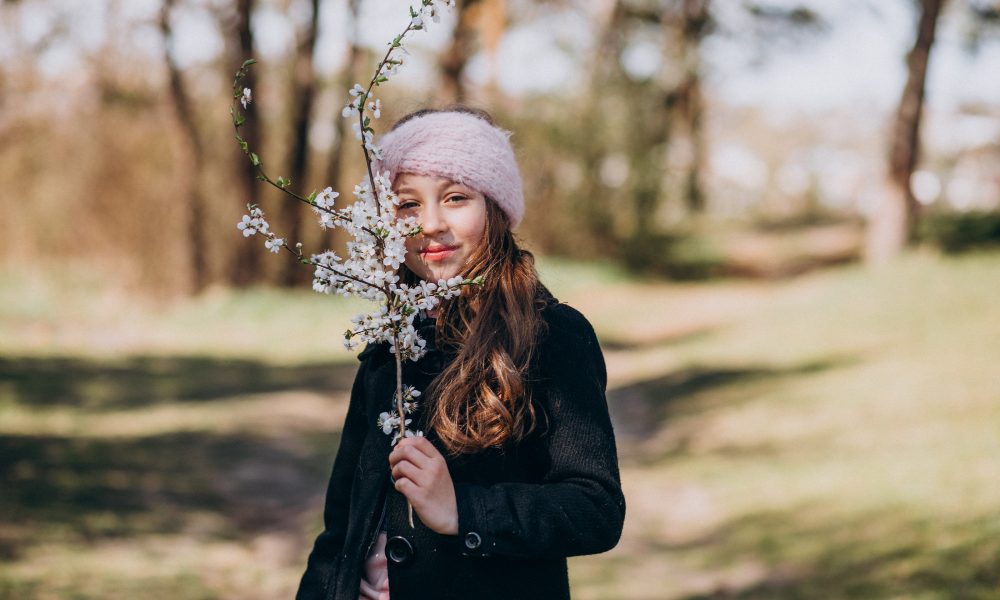 Девушка на прогулке в парке с цветущей веткой в руках.