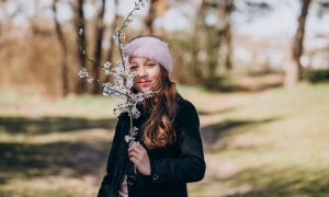 Девушка на прогулке в парке с цветущей веткой в руках.