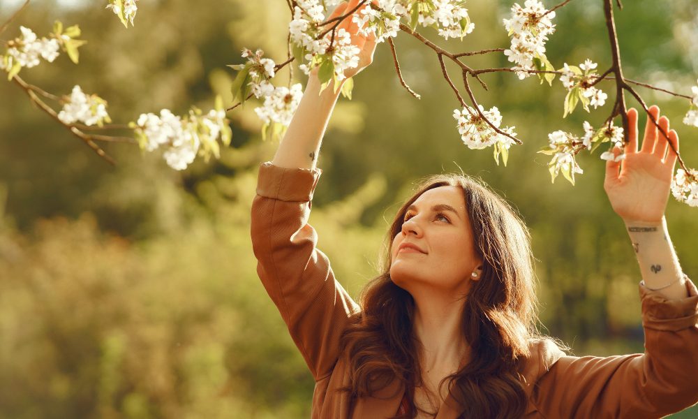 Девушка рассматривает цветущие ветки, подняв голову.