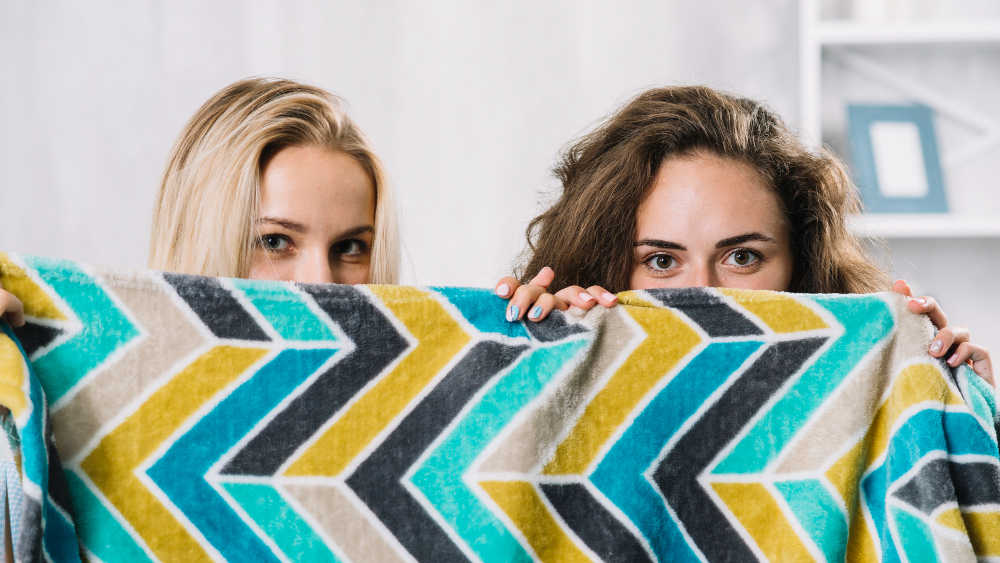Дае девушки выглядывают из-за пестрого покрывала
