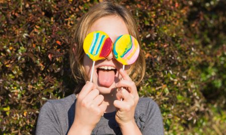 Девушка фотографируется, прикрыв глаза яркими леденцами на палочке.