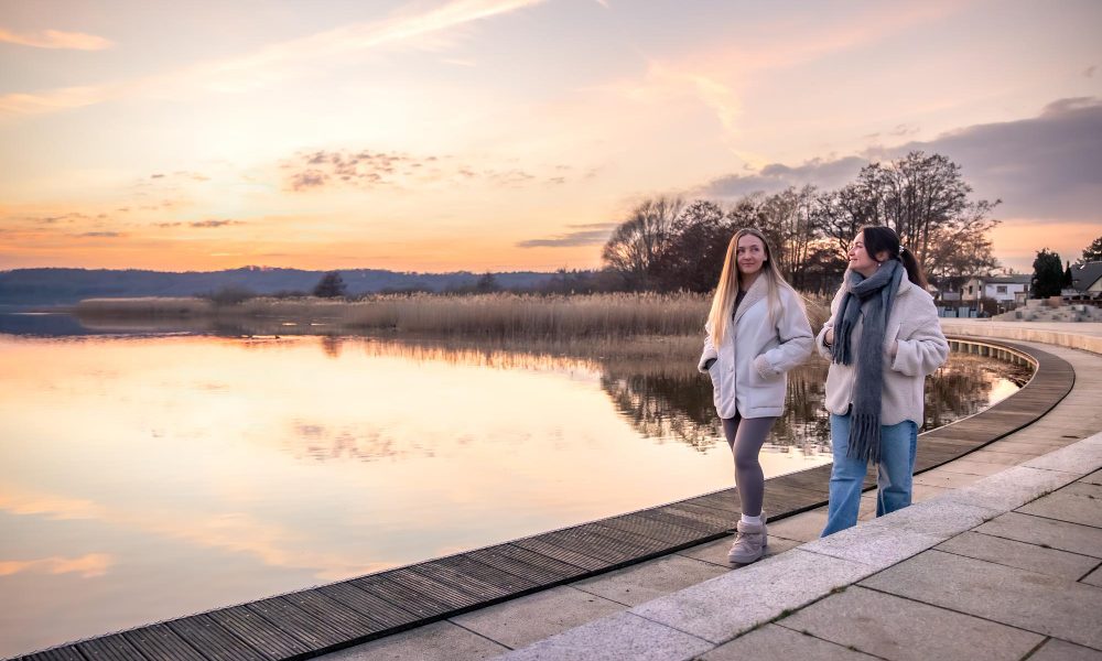 Две девушки гуляют по набережной в парке весной.