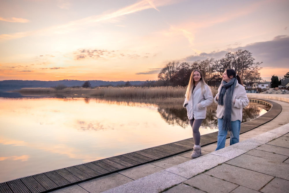 Две девушки гуляют по набережной в парке весной.