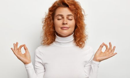 Рыжеволосая девушка в белой водолазке приняла позу спокойствия