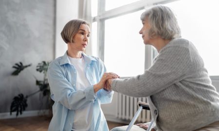 молодая женщина разговаривает с пожилой, держа ее руки в своих