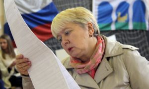 Женщина с бюллетенями в руках на избирательном участке.