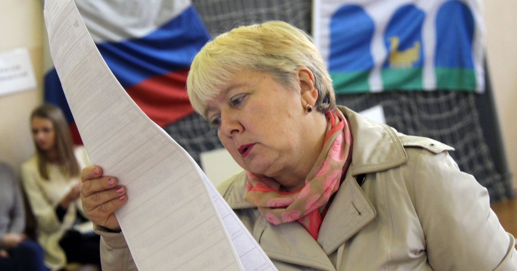 Женщина с бюллетенями в руках на избирательном участке.