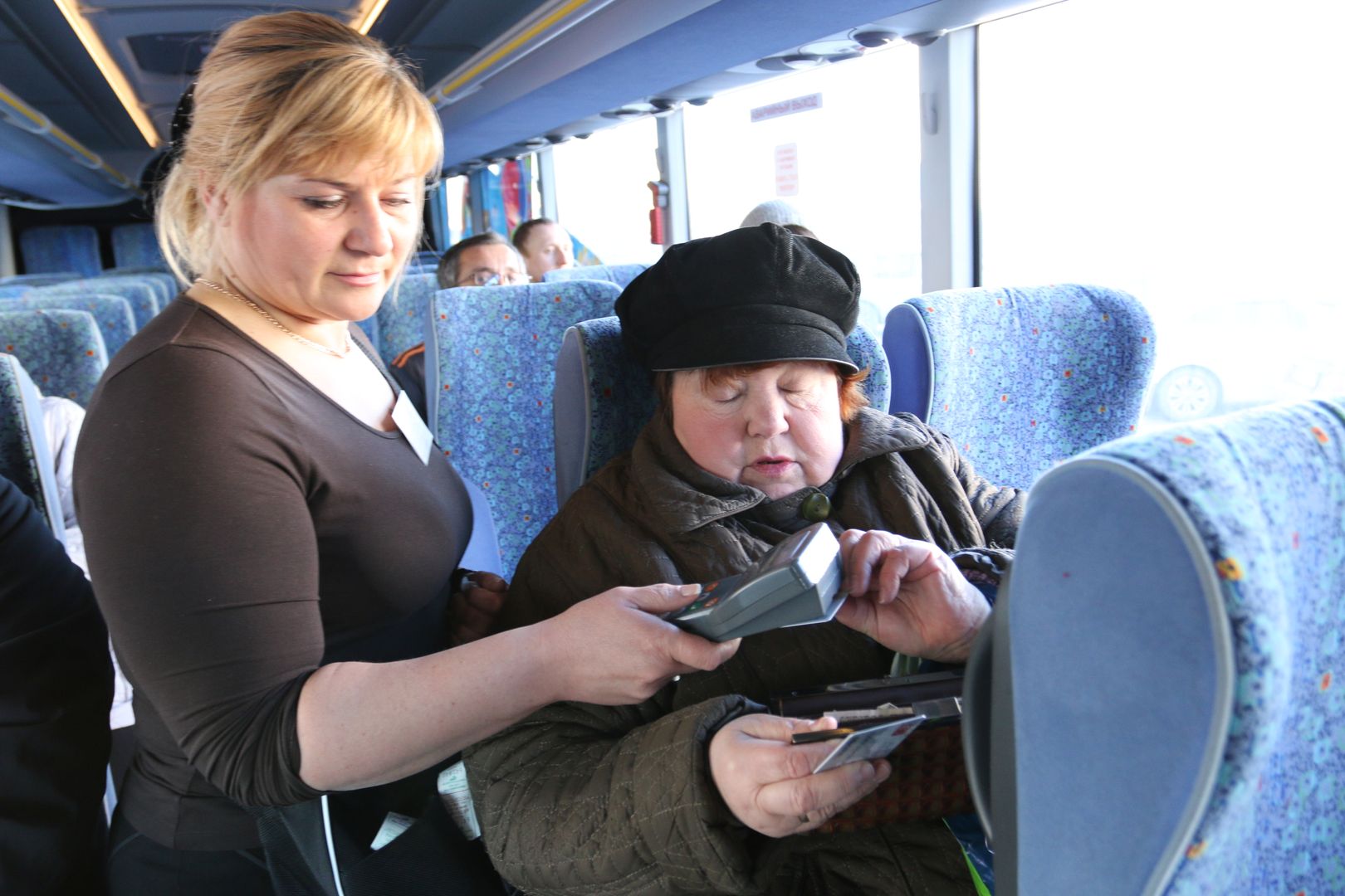 Контролер обилечивает пассажирку в автобусе.