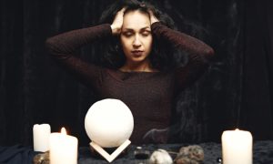 Темноволосая женщина за столом с мистическими атрибутами.