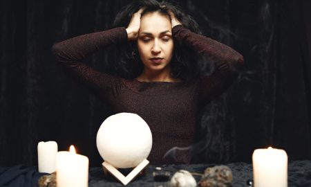 Темноволосая женщина за столом с мистическими атрибутами.