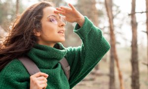 Девушка в зеленом свитере и очках смотрит вдаль.