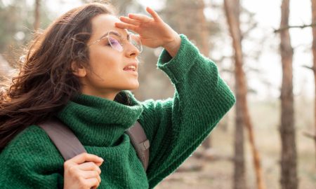 Девушка в зеленом свитере и очках смотрит вдаль.