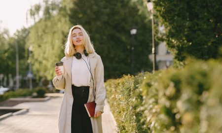 Девушка со стаканчиком кофе гуляет весной в парке.