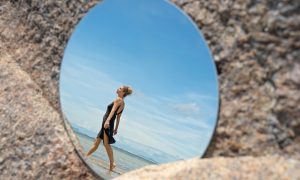 Идущая по берегу девушка отражается в зеркале.