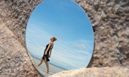 Идущая по берегу девушка отражается в зеркале.