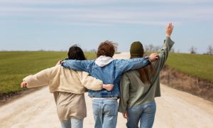 Трое друзей идут по дороге, обнявшись за плечи.