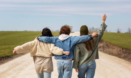 Трое друзей идут по дороге, обнявшись за плечи.