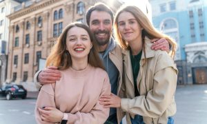 Две девушки и парень улыбаются, гуляя по весеннему городу.