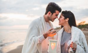 Мужчина и женщина на берегу с накинутыми на плечи пледами.