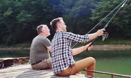 Пожилой и молодой мужчины рыбачат у реки.