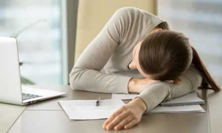 Уставшая девушка опустила голову на стол в офисе.