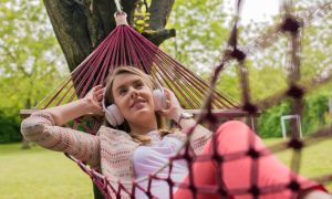 Девушка слушает музыку в наушниках, лежа в гамаке в весеннем саду.