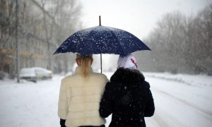 Женщины идут под зонтом во время снегопада