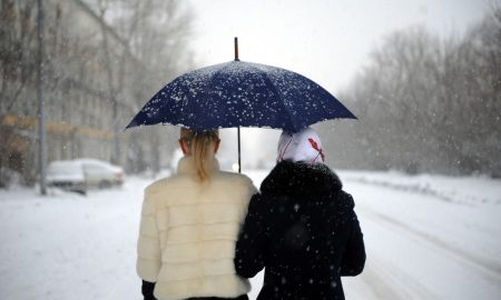 Женщины идут под зонтом во время снегопада
