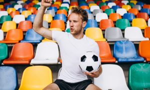 Молодой футболист на трибунах наблюдает за игрой.