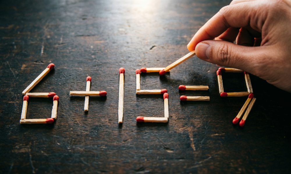 Арифметическое уравнение 6+15=9, выложенное из деревянных спичек на тёмной поверхности.