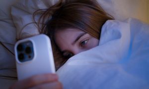 Девушка лежит в кровати со смартфоном в руках.