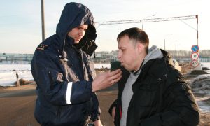 Инспектор ГИБДД проверяет водителя на уровень содержания алкоголя в крови с помощью алкотестера